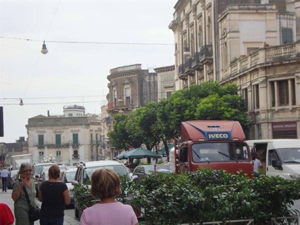 Red Iveco truck in traffic among baroque buildings and pedestrians on a square