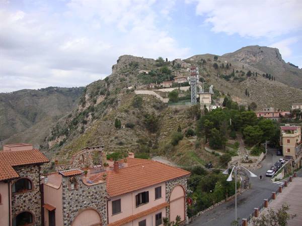 Brick rooftops and stone houses beneath hillside cable car, Taormina