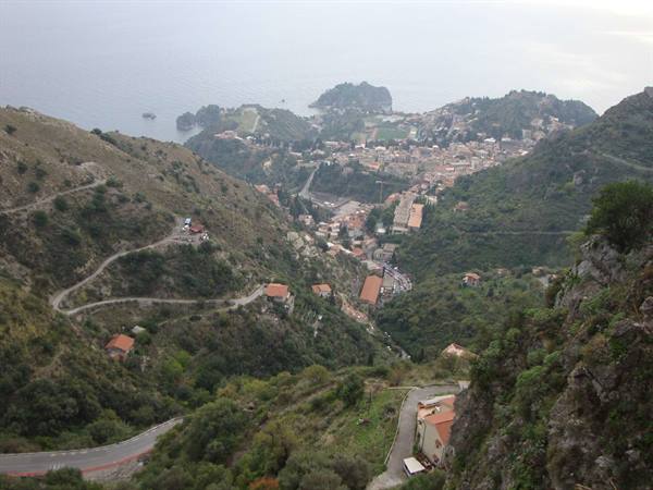 Winding road through green hills descends to a coastal town under grey sky