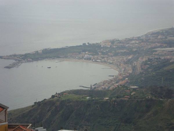 Giardini Naxos bay with curved sandy beach, boats and hazy hillside houses