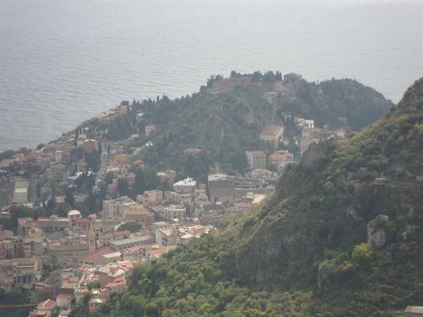 Taormina: rooftops among green hills with hazy sea behind