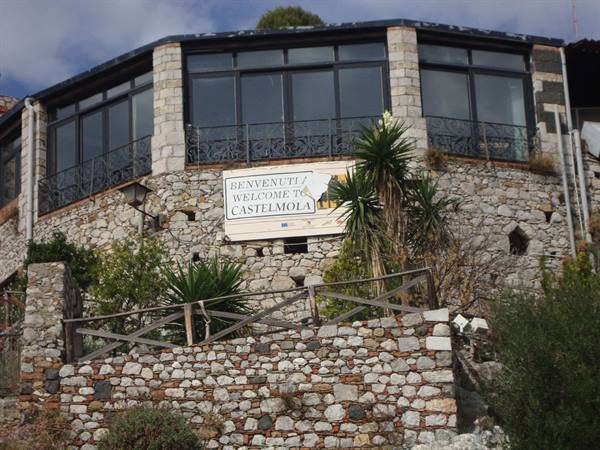 Stone building in Castelmola with welcome sign, plants and wooden fence
