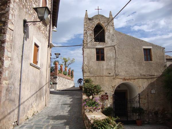 Stone alley with small bell-tower church among old sunlit village houses