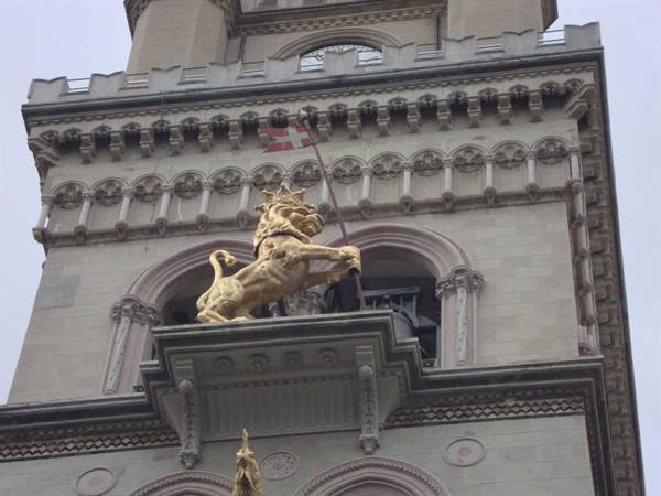 Gilded crowned lion holding a banner on a stone clock tower against grey sky
