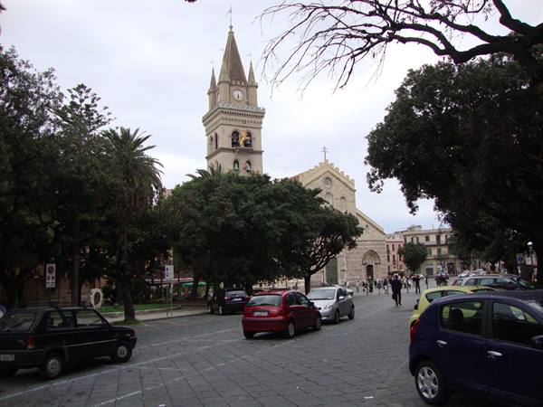 Messina cathedral with its bell tower, parked cars and pedestrians under a grey sky