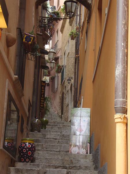 Stone stairway between ochre houses, hanging lanterns and painted ceramics, Taormina