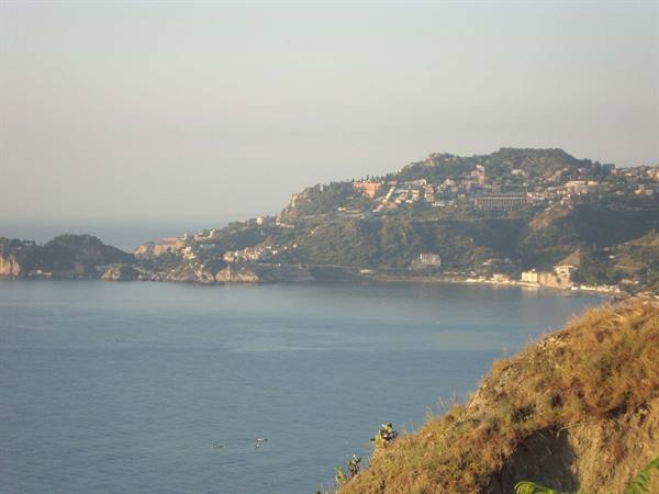 Hillside houses over calm sea, golden haze near Taormina