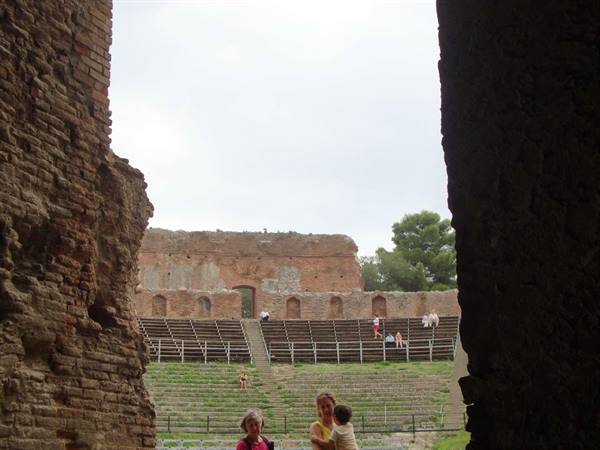 Visitors among ancient Roman brick theater ruins with grassy tiers
