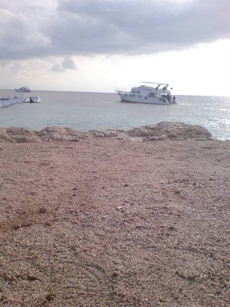 White boat approaches a reddish pebble beach under cloudy sky