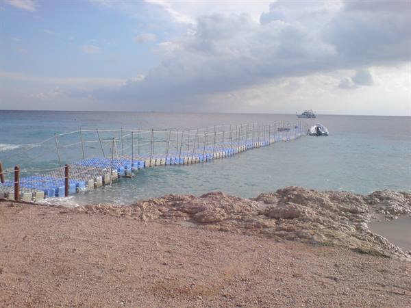 Blue floating pontoon pier over turquoise sea, a boat resting near rocky beach