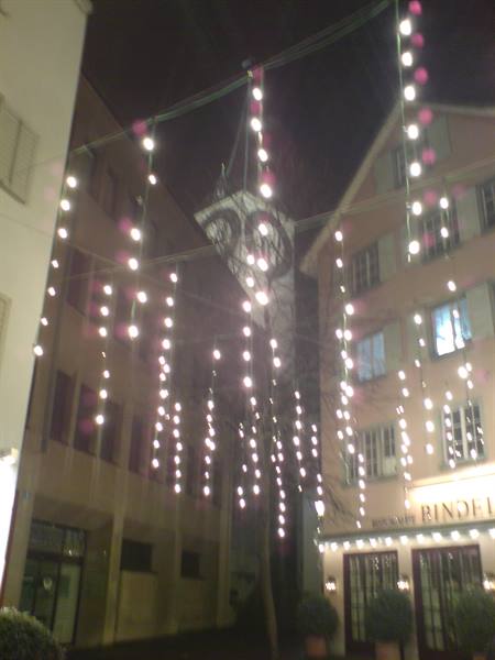 Pink hanging lights between buildings at night, lit restaurant sign