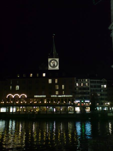 At night St. Peter's clock tower reflects on the Limmat river in Zurich