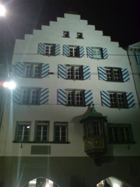 Historic facade at night, zigzag blue-and-white shutters, wooden oriel window