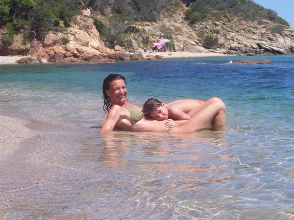 Mother and child playing in clear shallow water by Villasimius rocks