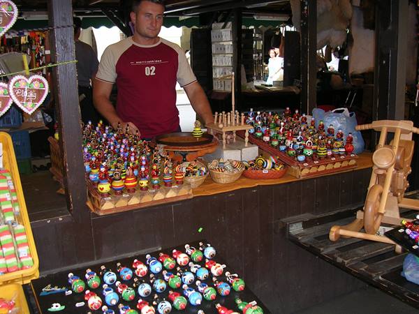 Vendor surrounded by painted wooden toys and figurines at market stall