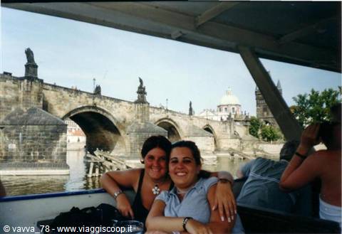 Two smiling tourists on a boat on the Vltava in front of Charles Bridge