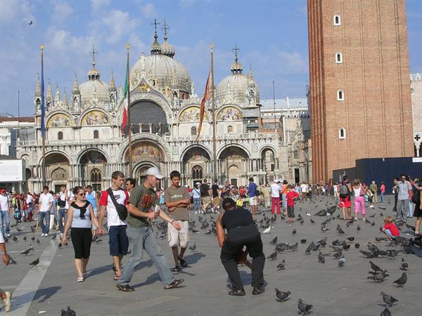 Tourists and pigeons in St Mark's Square before the golden Basilica and Venice bell tower