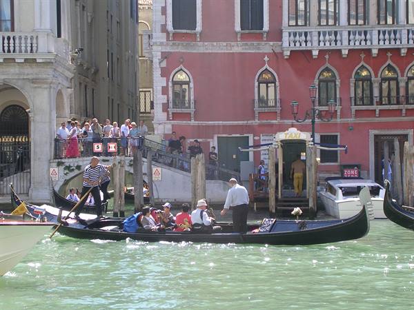 Gondolier carrying tourists on a black gondola past Venice palaces