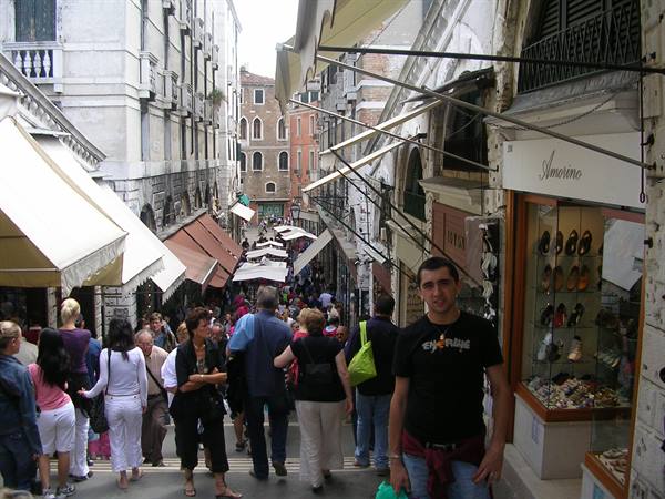 Crowd on a busy Venice street lined with awnings and shoe shops