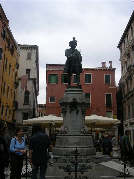 Bronze statue of Carlo Goldoni on a Venetian square, people passing under gray sky
