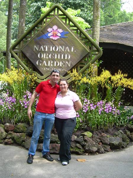 Couple in front of the wooden National Orchid Garden sign among yellow and purple orchids