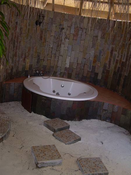 White jacuzzi tub on sandy floor, stone walls and thatched roof