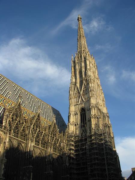 Gothic spire of St. Stephen's Cathedral, Vienna, colorful tiled roof, scaffolding, sunlight