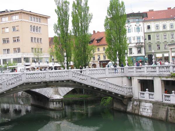 Stone bridge with balustrade over the river in Ljubljana, people among buildings