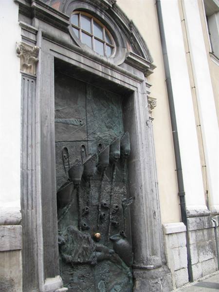 Sculpted bronze church door with relief figures, grey stone frame, soft daylight