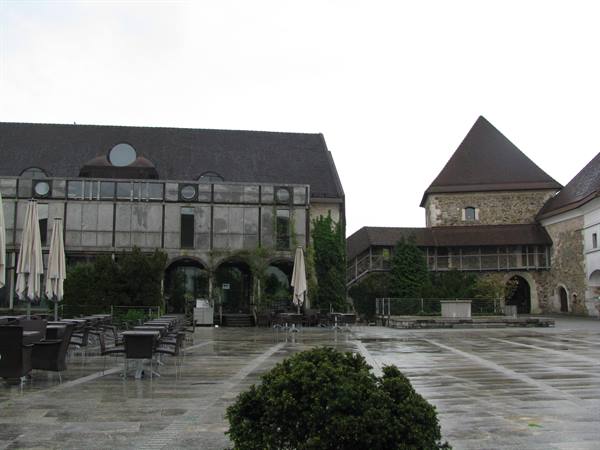 Wet castle courtyard: closed umbrellas over empty tables, medieval stone walls