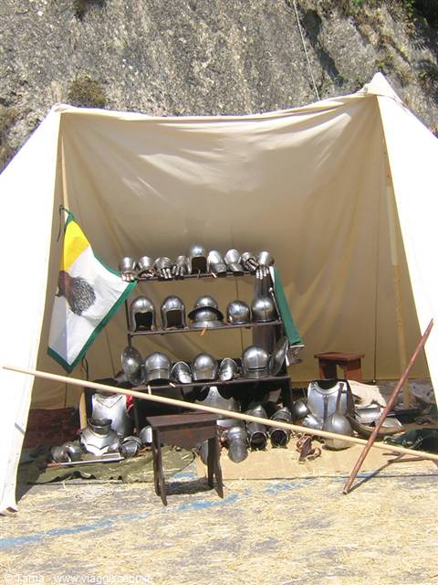 Medieval tent displaying metal armor and helmets on wooden shelves