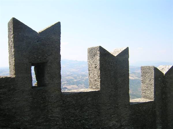Stone battlements of a medieval tower above sunlit hills