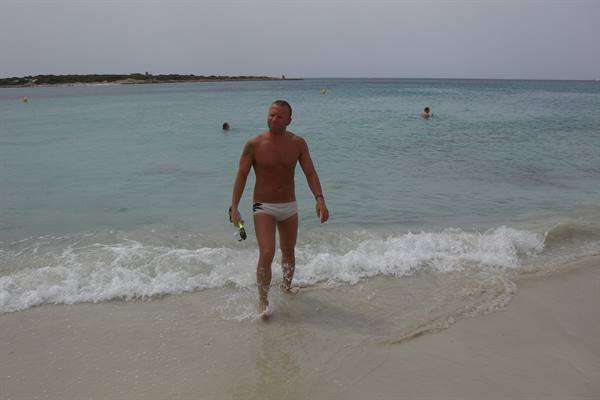 Man in white swim trunks walks out of turquoise sea with snorkel mask, sandy beach