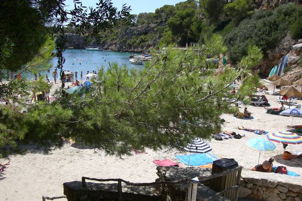 sandy cove with pines, colorful umbrellas, swimmers and boats on turquoise water