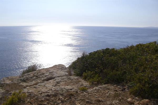 Limestone rock and Mediterranean shrubs over the sea, sunlight reflecting on water