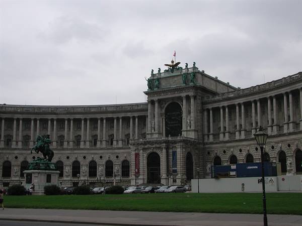 Vienna, Hofburg: curved stone facade with green statues, equestrian monument, grey sky