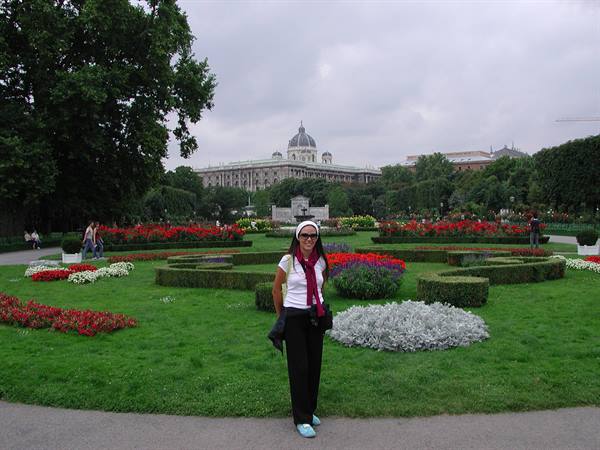 Woman smiling among flower beds in Vienna's Volksgarten, Natural History Museum behind