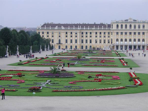 Schönbrunn gardens: flowerbeds before the yellow palace, visitors strolling under gray sky