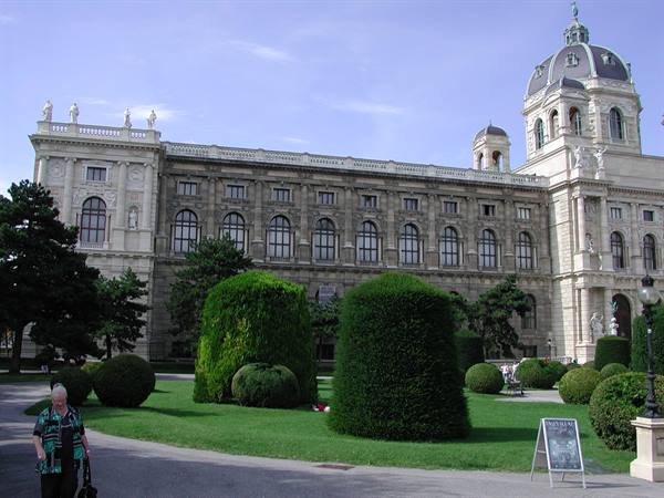 A lady walks past the Kunsthistorisches Museum, green hedges and dome