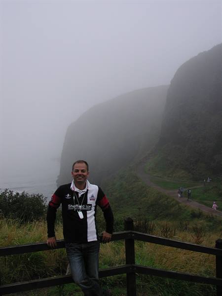 Man leaning on wooden fence by foggy cliff path above the sea