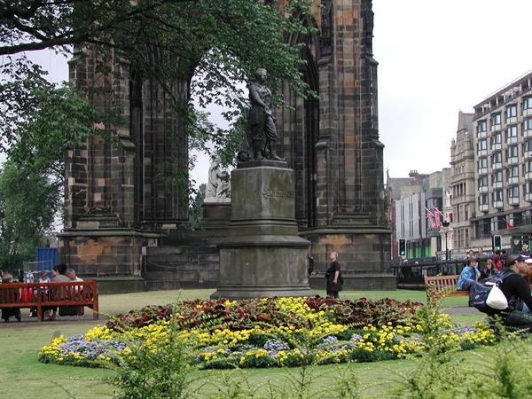 Walter Scott statue before the Scott Monument, flowerbeds, benches and tourists in Edinburgh