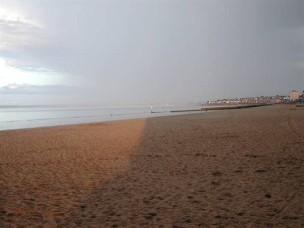 Wet sand at dawn, pier and seaside buildings under cloudy sky