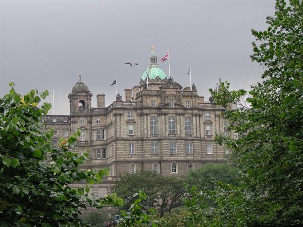 Stone building with green copper dome and flags, framed by trees under grey sky