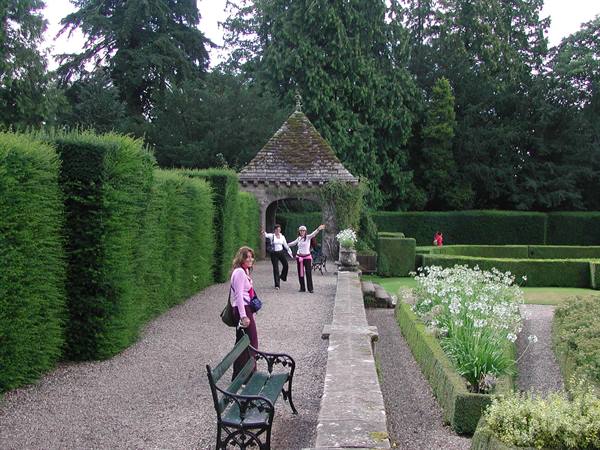 Tourists on the gravel garden path, among clipped hedges and a stone pavilion