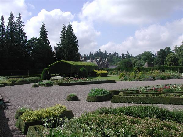 Garden with clipped box hedges, gravel paths and a castle behind trees