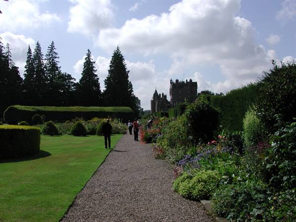 Gravel path between flowerbeds and topiary hedges, visitors toward Glamis Castle