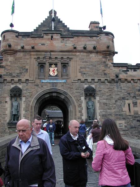 Tourists walk through the stone gatehouse of Edinburgh Castle with statues and flags