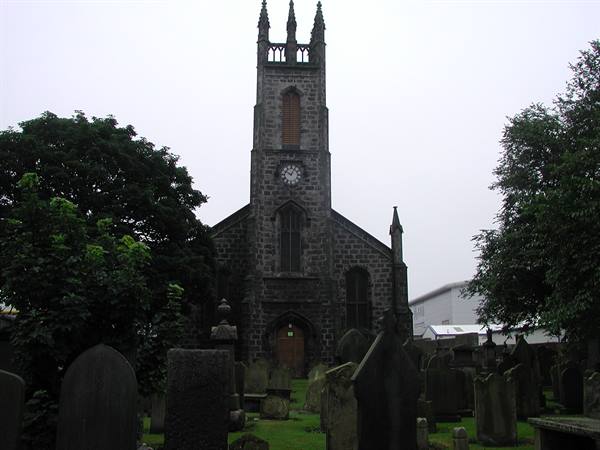 Grey stone church with clock tower, surrounded by gravestones