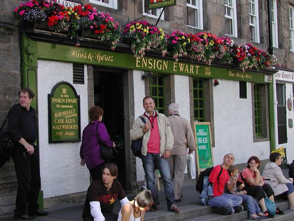 Tourists sitting outside the Ensign Ewart pub in Edinburgh, flowers above the sign