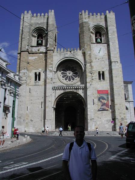 Tourist in front of Lisbon Cathedral, stone facade with rose window and two bell towers, sun
